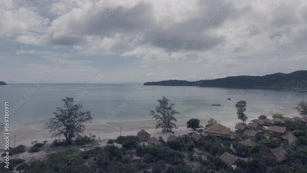Drone view : Bungalows along white sand beach with rainforest view under cloudy sky Drone view : Bungalows along white sand beach with rainforest view under cloudy sky