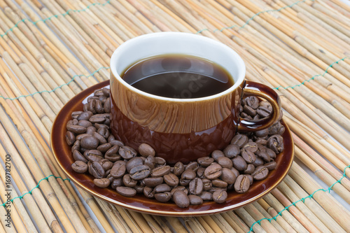 Hot black coffee in a dark brown old fashioned cup on a rustic texture background.
Roasted coffee beans inside the saucer. Hot steam on the coffee.
