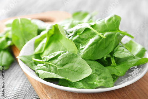 Plate with fresh spinach leaves on wooden board