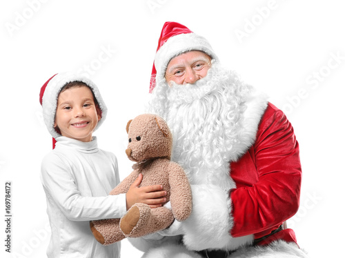 Authentic Santa Claus giving teddy bear to cute boy in Christmas hat on white background