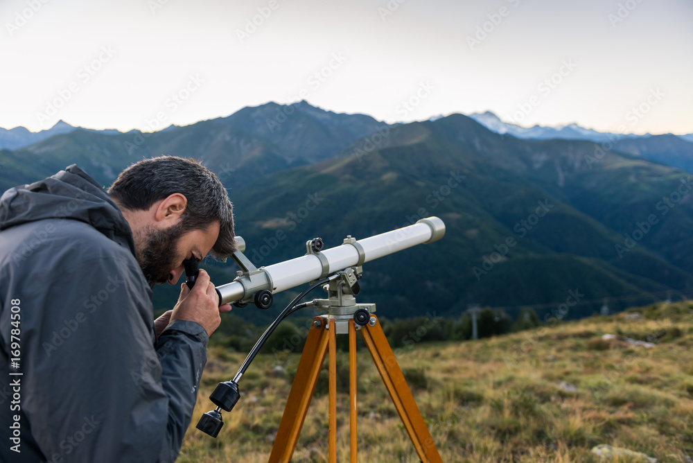 Man looking through telescope mountain peaks in summer evening at sunset on mountain outdoor.