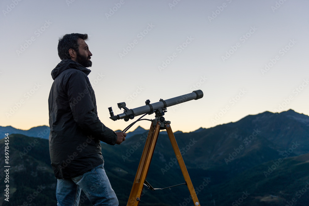Man looking at mountain peaks near telescope in summer evening at sunset on mountain outdoor.