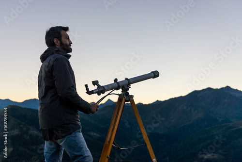 Man looking at mountain peaks near telescope in summer evening at sunset on mountain outdoor.