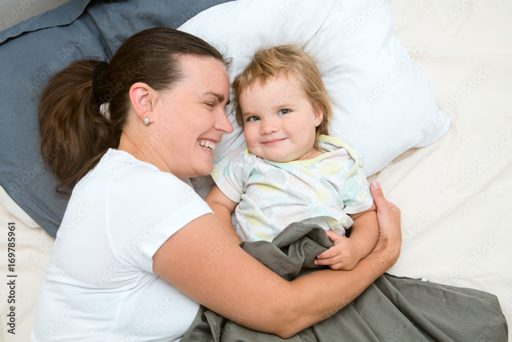 Happy smiling mother and baby playing and laughing lying on bed at home.Happy Family having fun together. Happy smiling mother and baby playing and laughing lying on bed at home.Happy Family having fun together.