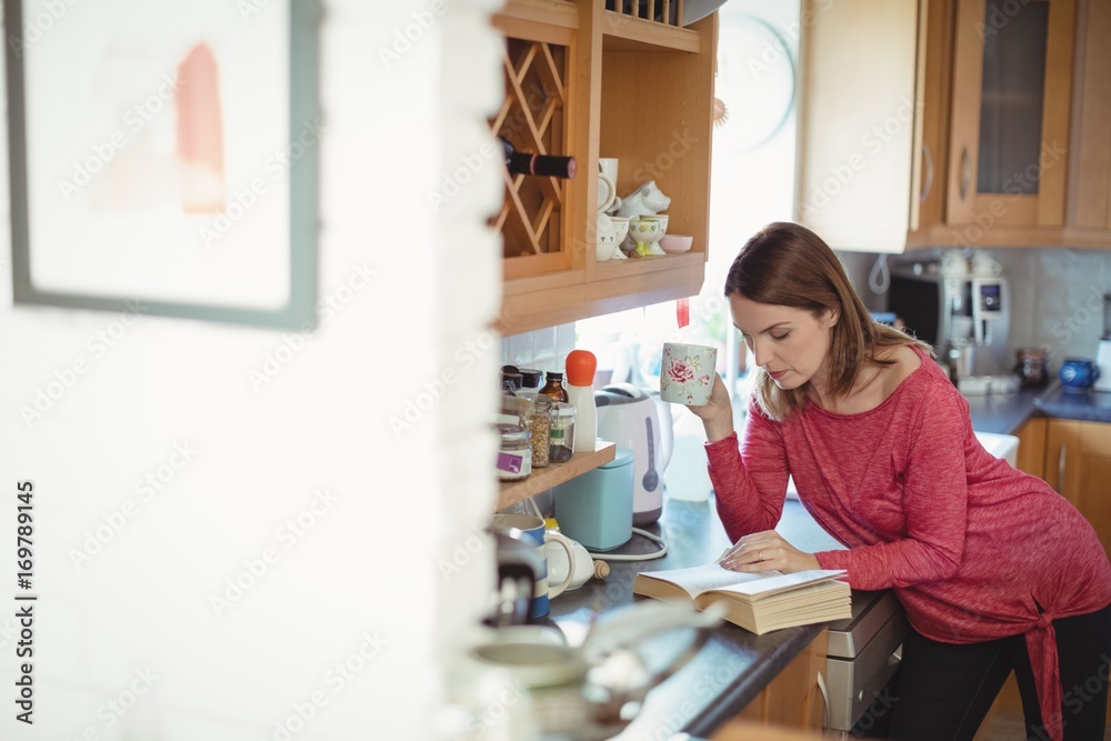 Woman reading a book while having coffee in kitchen Woman reading a book while having coffee in kitchen