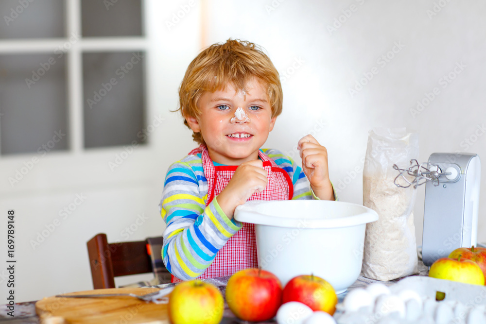 Funny blond kid boy baking apple cake indoors Funny blond kid boy baking apple cake indoors