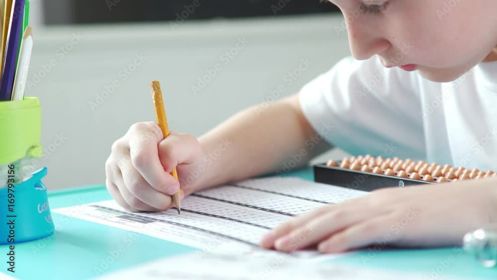 An inquisitive and diligent boy does homework and math. Pupil is healed by mental arithmetic, using special scores. Close-up: children's hands write with a pencil and use accounts of Abakus (Soroban).