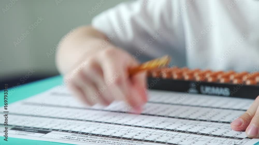 An inquisitive and diligent boy does homework and math. Pupil is healed by mental arithmetic, using special scores. Close-up: children's hands write with a pencil and use accounts of Abakus (Soroban).