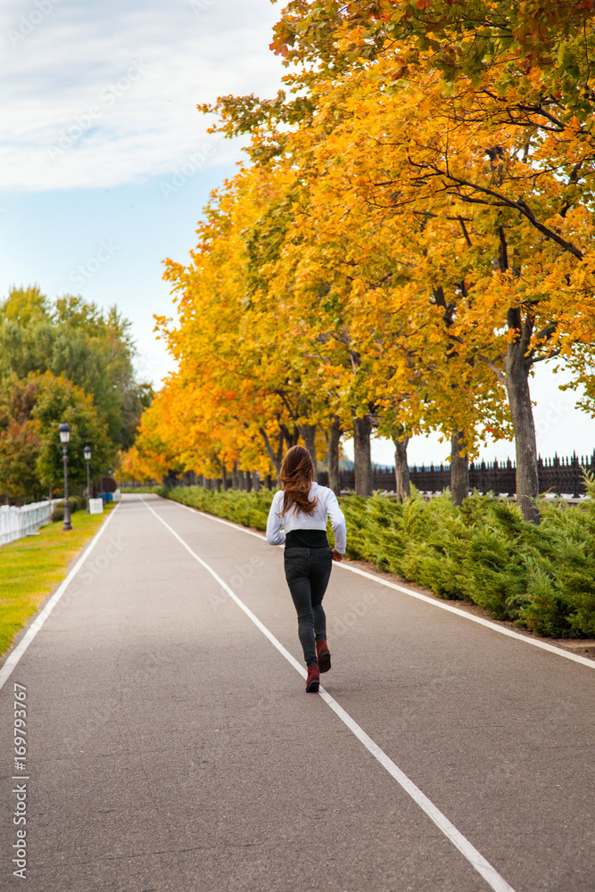 Young adult woman running in autumn forest. Girl jogging in road.