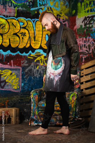 A creative, unusual red-haired man in designer clothes and tunnels in his ears, posing in the studio.