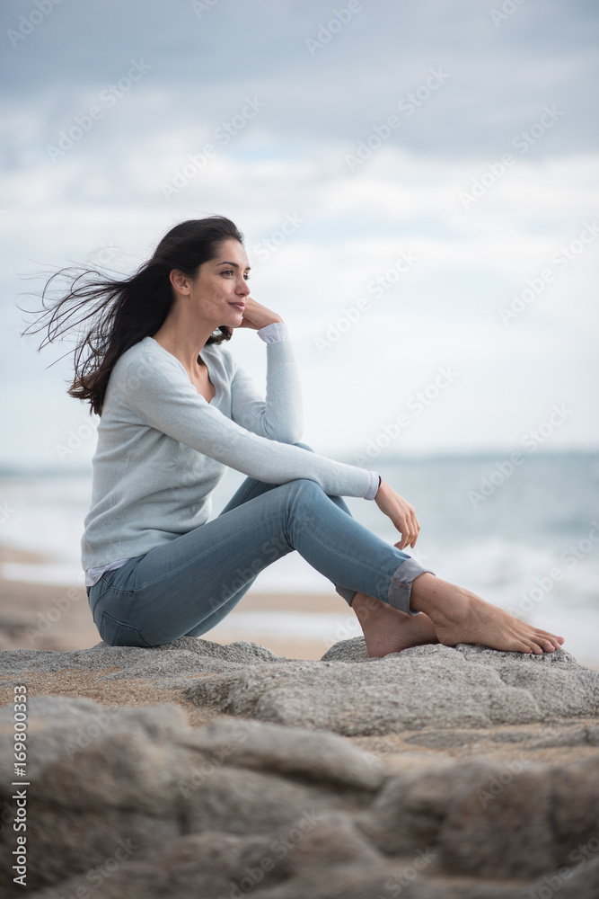 A beautiful young brunette sitting on a rock at the beach A beautiful young brunette sitting on a rock at the beach