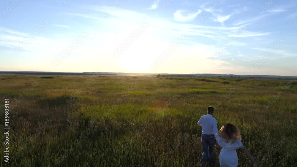 Aerial photography of a young couple running across the field towards the sunset Aerial photography of a young couple running across the field towards the sunset