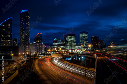 Cityscape of London at night in Canary Wharf, The city’s second largest financial center, with light trails on the freeway leading to the modern skyscrapers of this district, a landmark of England, UK