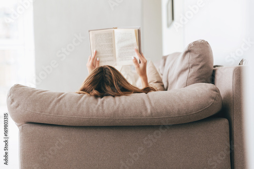 Back view of woman lying and reading book