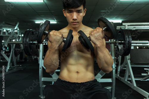 Fitness man in training showing exercises with dumbbells in gym