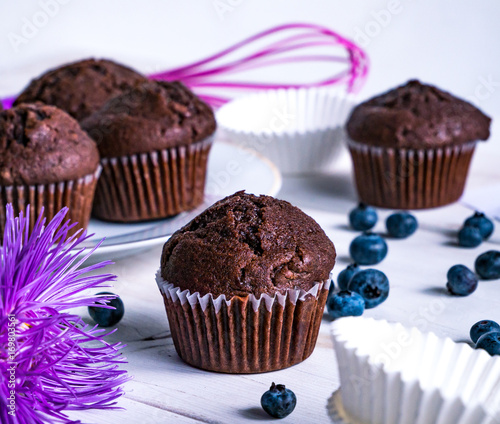 Close-up of chocolate muffins on a white wooden table with various decorations.