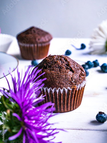 Close-up of chocolate muffins on a white wooden table with various decorations.