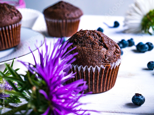 Close-up of chocolate muffins on a white wooden table with various decorations.