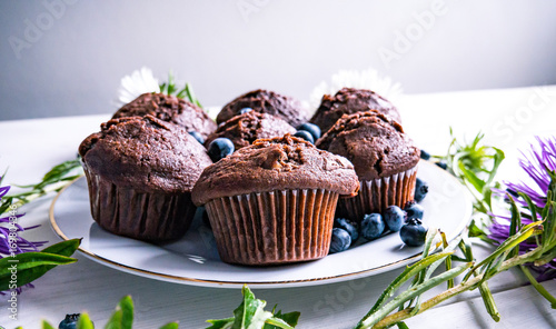 Close-up of chocolate muffins on a white wooden table with various decorations.