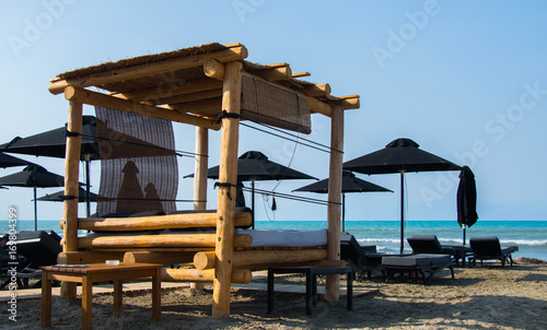 beutiful beach with  wooden big sun bed and black  and white beach umbrellas and sun beds against turquise see and blue sky  © Magdalena