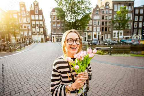 Photography Portrait of a young and happy woman holding a bouquet of pink tulips standing ou