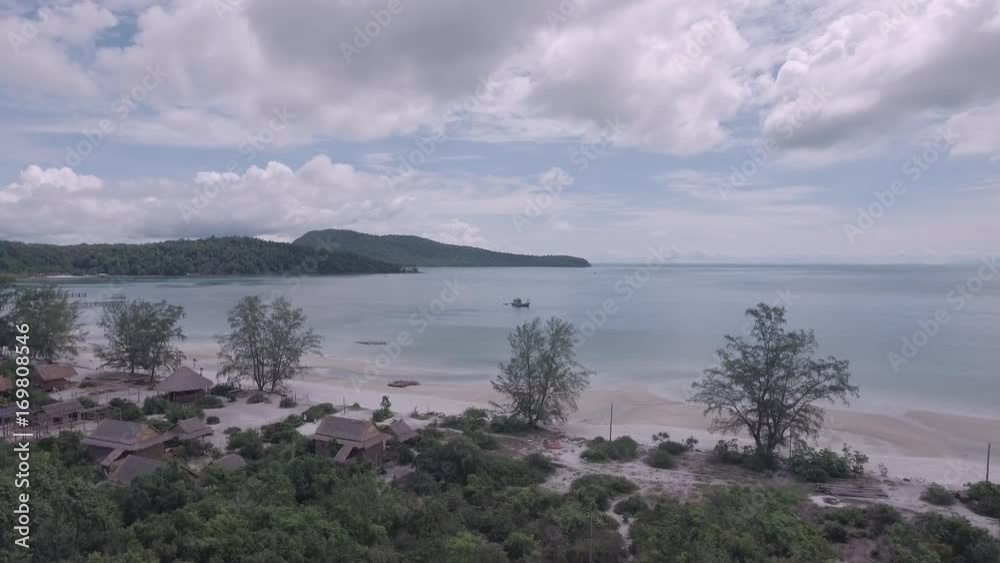 Drone view : flying over bungalows along sand beach with rainforest view and towards a fishing boat off the coast Drone view : flying over bungalows along sand beach with rainforest view and towards a fishing boat off the coast
