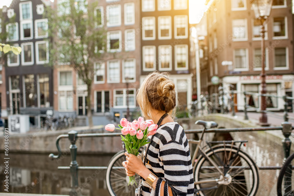 Naklejka premium Styl życia portret kobiety idącej z bukietem różowych tulipanów w pobliżu kanału wodnego w mieście Amsterdam