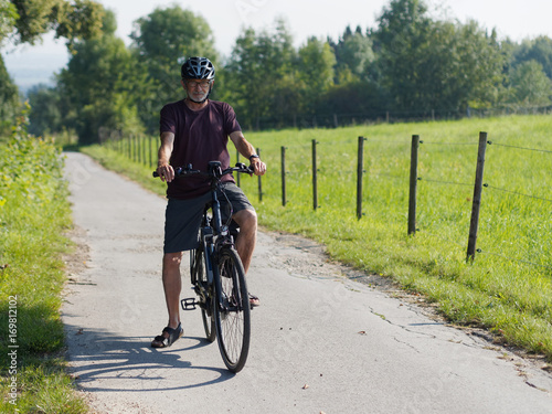 Fototapeta Naklejka Na Ścianę i Meble -  Älterer Mann macht Radtour mit E-Bike in schöner Landschaft