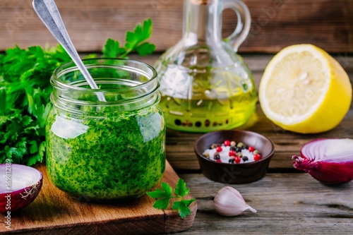 Traditional green chimichurri sauce with fresh parsley, red onion, garlic, olive oil in glass photo