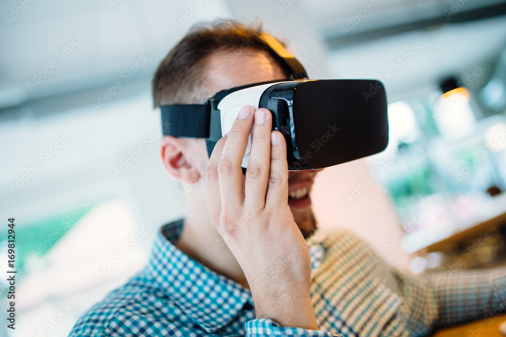 Young handsome man sitting in cyber cafe and using virtual reality headset or glasses.