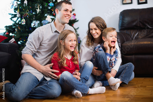 Young happy family sitting by Christmas tree at home © JackF