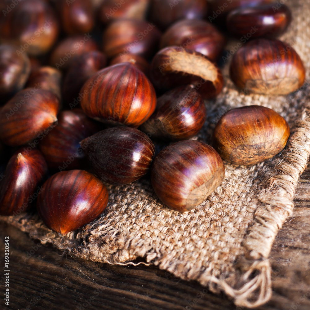 Fototapeta premium Ripe chestnuts on old wooden table and sack napkin close up with copy space. Roasted Chestnuts for Christmas.