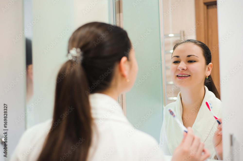 Image of pretty female brushing her teeth in front of mirror in the morning Image of pretty female brushing her teeth in front of mirror in the morning