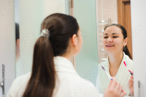 Image of pretty female brushing her teeth in front of mirror in the morning
