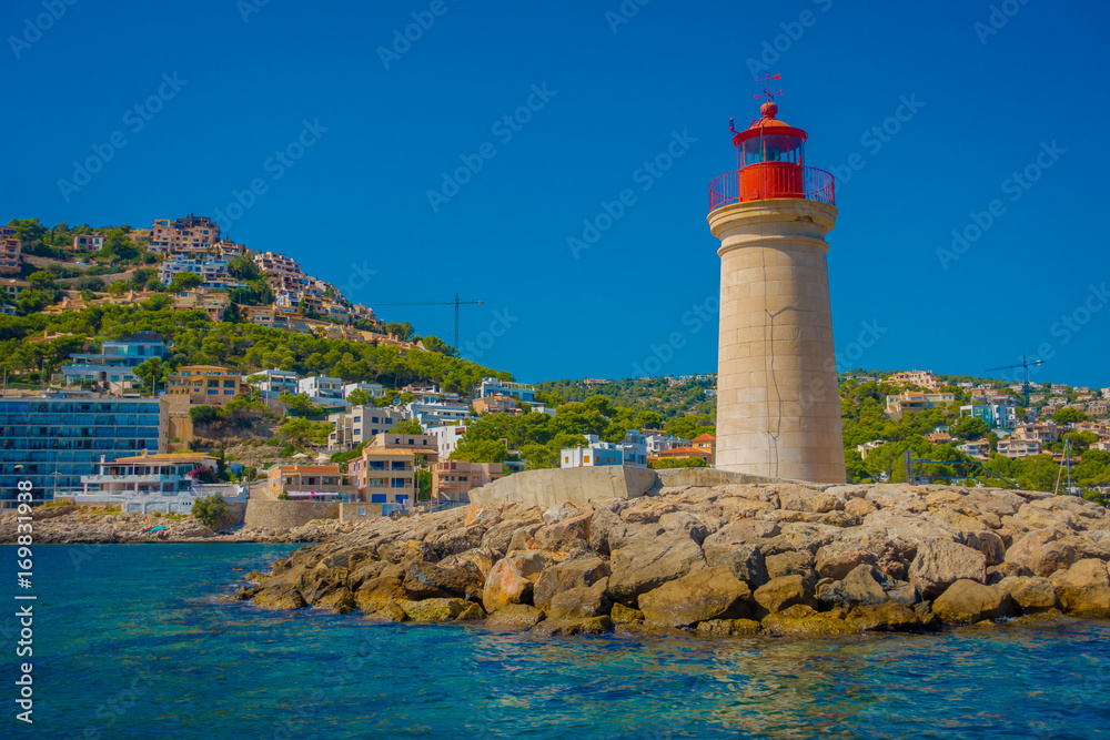 Beautiful view of Mallorca balearic islands, with a lighthouse and some buildings in the mountain in the horizon, with gorgeous blue water and a beautiful blue sky, in Spain