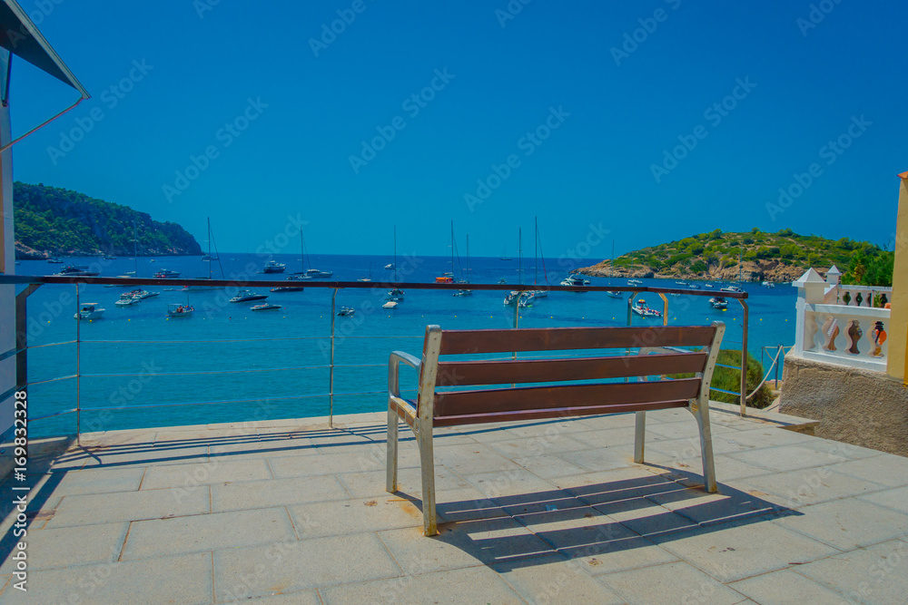 Beautiful sunny day in Sant Elm, with a public chair to enjoy the view in Majorca, with people enjoying the water, in Spain