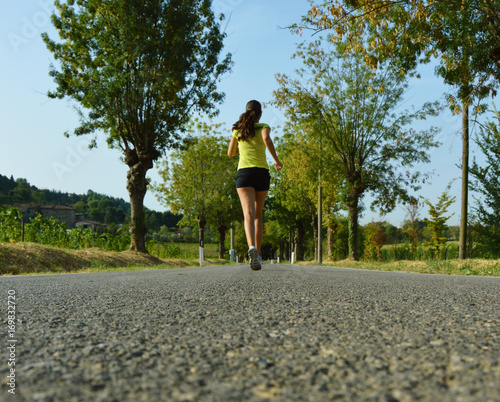 Fitness woman running on asphalt road. Long view.