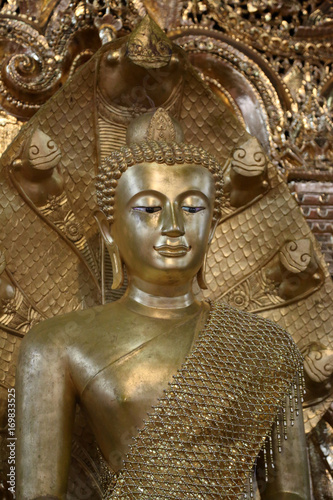 Antique gold Buddha statue covered in golden robes at temple in Myanmar.