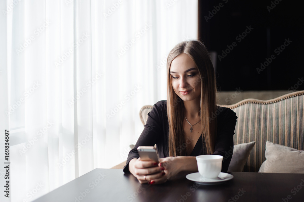 Young attractive girl sitting alone near big window in coffee shop during free time Young attractive girl sitting alone near big window in coffee shop during free time