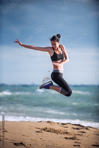 A young woman wearing sportswear is jumping on the beach