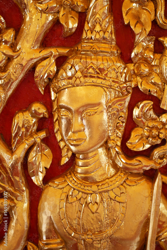 Fototapeta premium close-up male Thai angel statue filled with gold leaf isolated with red backgrounds, wooden crafting product painted with gold colors, guardian traditional souvenir