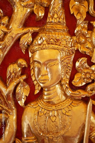 close-up male Thai angel statue filled with gold leaf isolated with red backgrounds, wooden crafting product painted with gold colors, guardian traditional souvenir