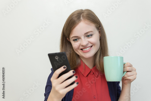 Young caucasian girl with a smart phone in one hand and a cup in another, smiling