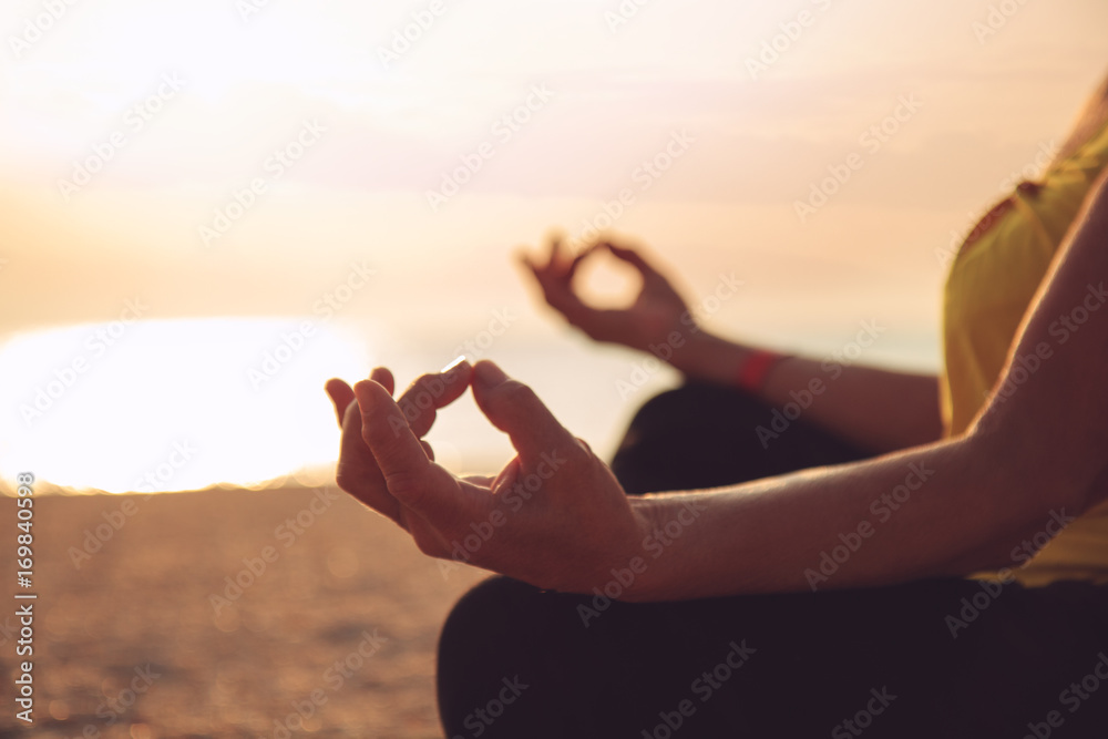 Hands of mature woman practicing yoga at lotus pose, at the sea beach