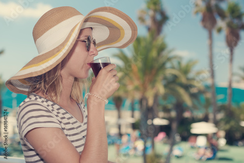 Attractive girl in bonnet hat drinking wine against wonderful sea view. Santa Susanna. Cataluna. Spain.