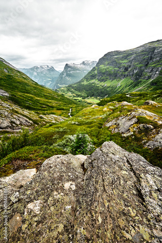 Path over green pasture in the mountains of Western Norway with snow on the summits and a dark cloudy sky