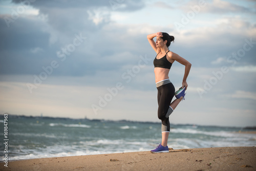 A young woman wearing sportswear is doing stretches on the beach