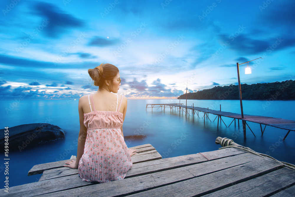 Young woman sitting on wood pier looking in the sea, back view.