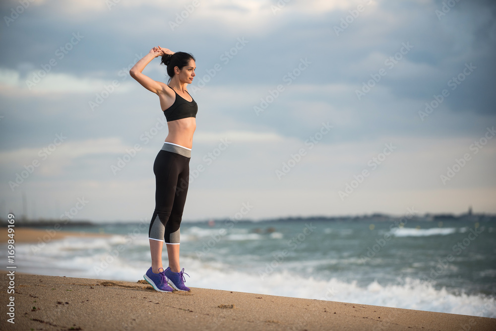 A young woman wearing sportswear is doing stretches on the beach