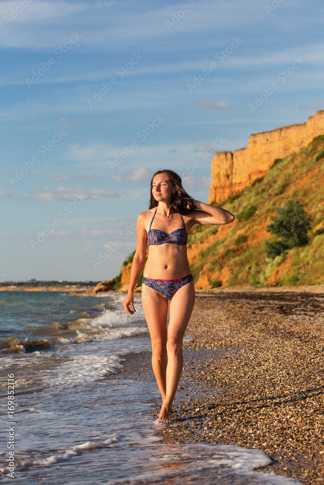 Slender woman in swimsuit walks in sea surf